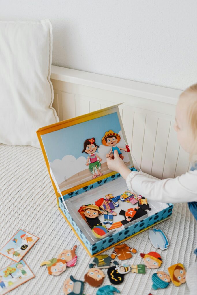 A young girl playing with a vibrant dress-up puzzle set on a bed, featuring cartoon characters.