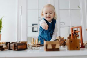 Smiling girl playing with wooden toys indoors, pointing and having fun.